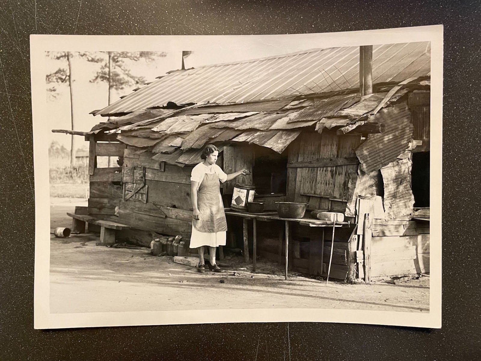 black and white photo of woman sanding in front of shack