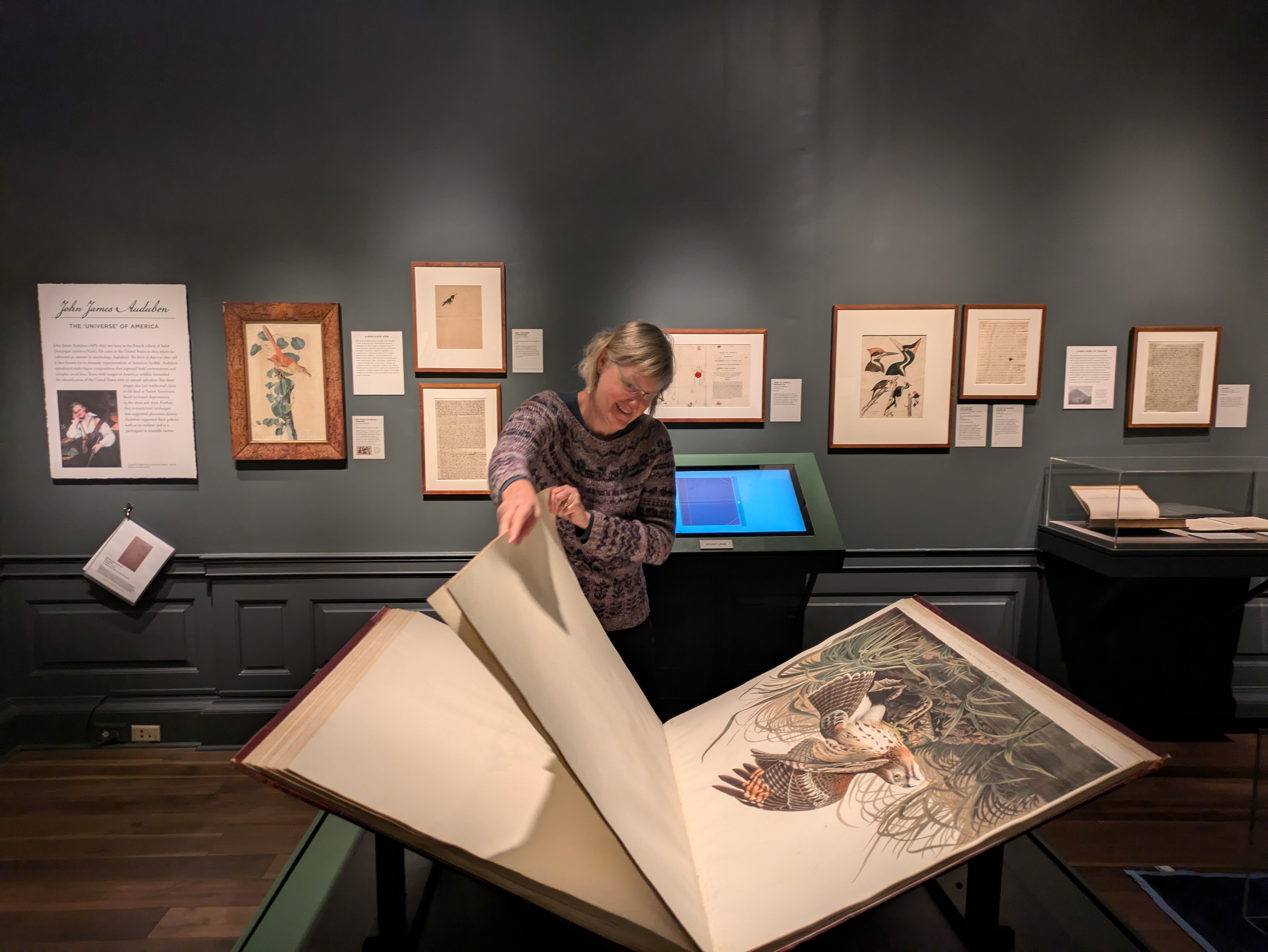 photo of woman turning page of large The Birds of America volume in exhibit